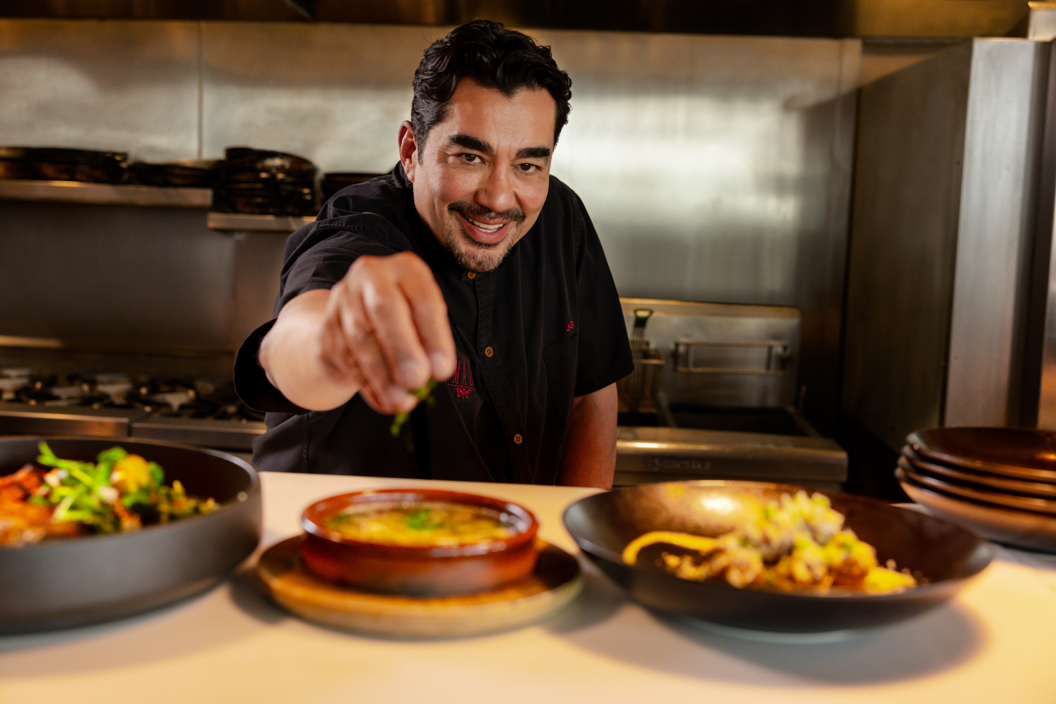 Chef José Garces smiling while garnishing a dish in the kitchen at Ocean Casino Resort.