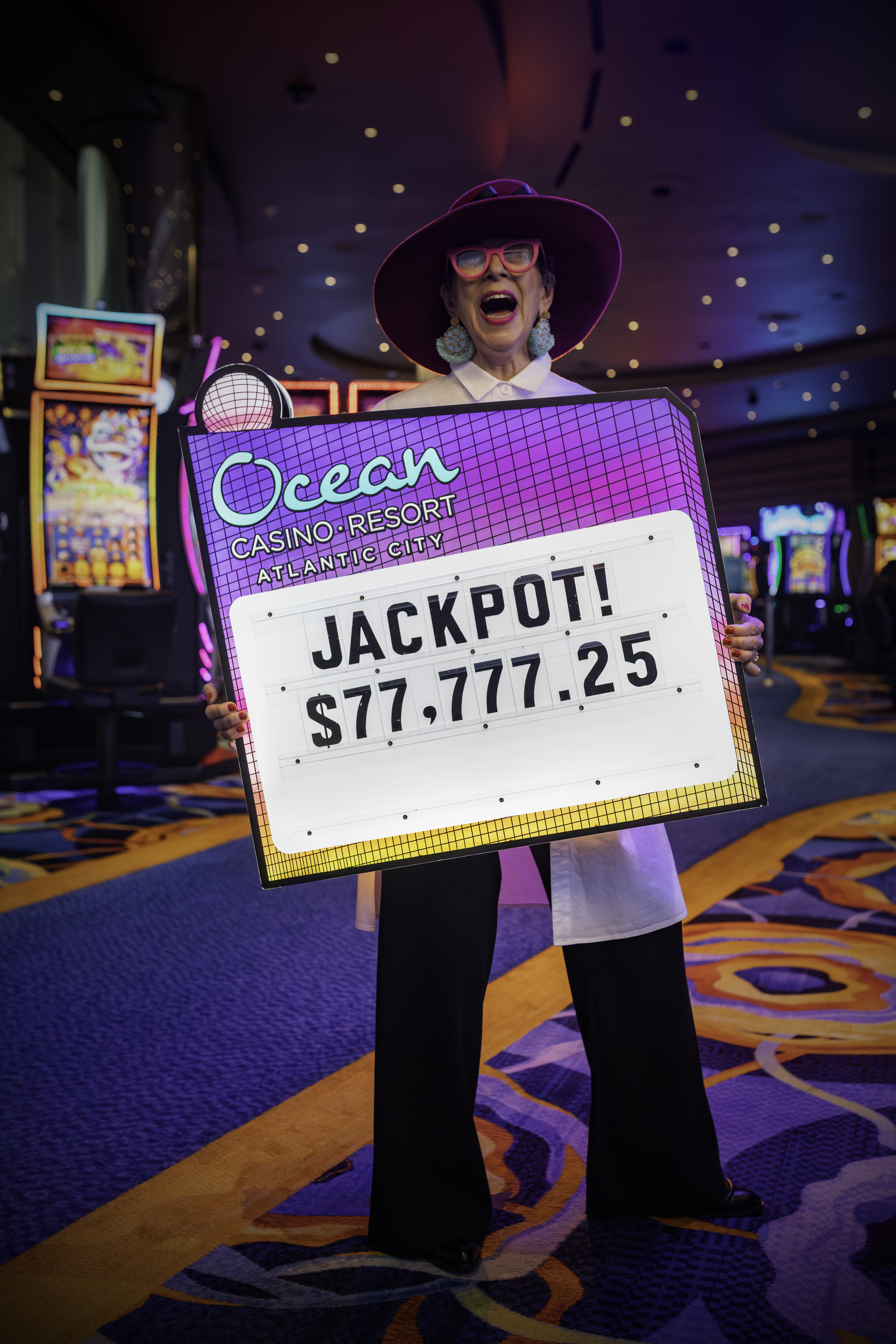 Guest celebrating a jackpot win of $77,777.25 at Ocean Casino Resort, holding a large retro-style prize sign with excitement.