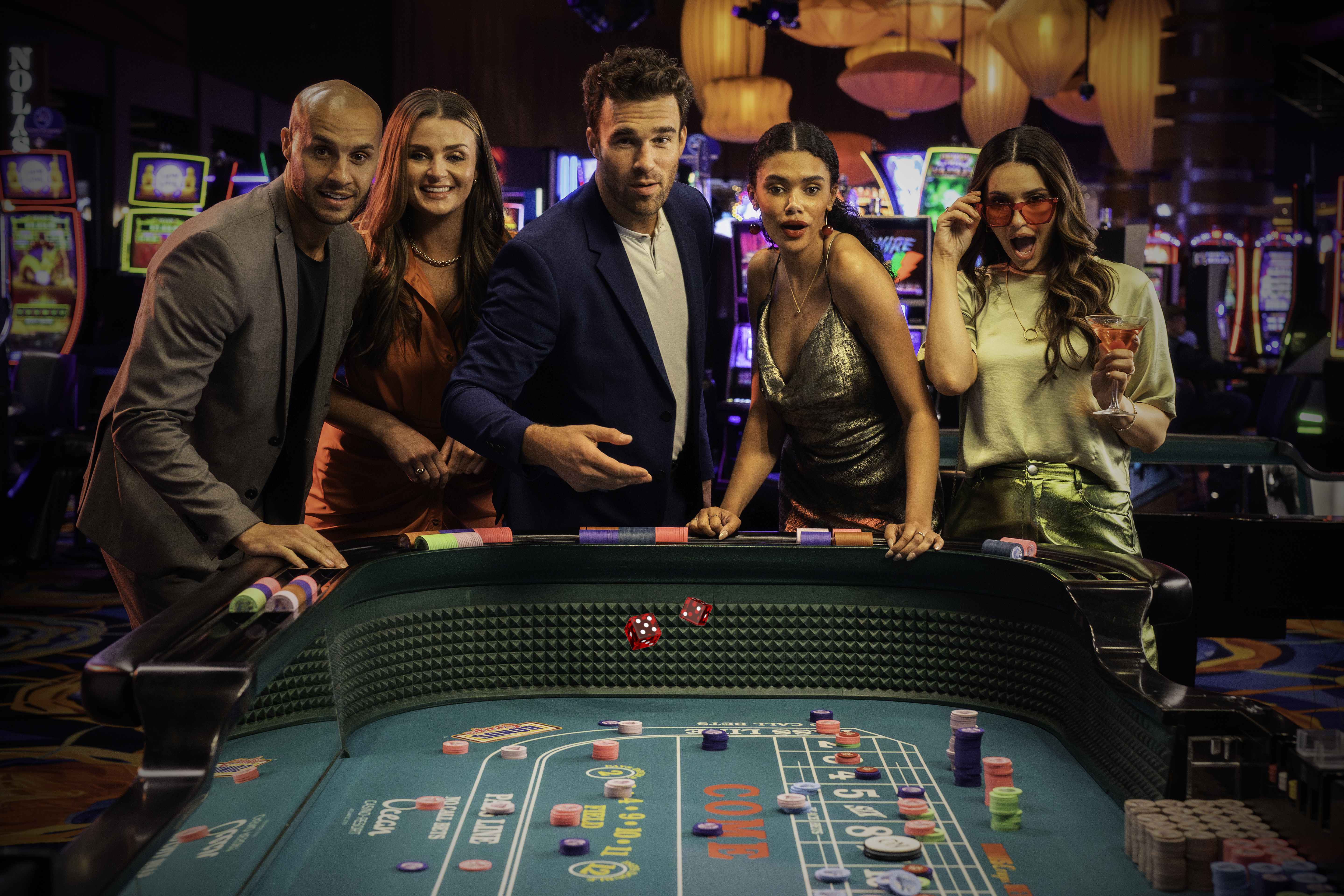 Group of friends excitedly watching dice roll across a craps table at Ocean Casino Resort, surrounded by slot machines and vibrant lights.